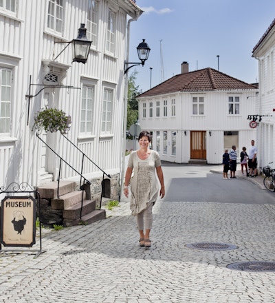 En kvinne går på brostein forbi en hvit bygning med museumsskilt utenfor