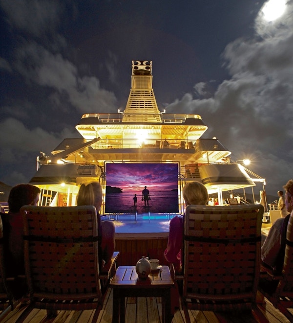 Kino på dekk av yacht om kvelden med tilskuere i behagelige stoler.