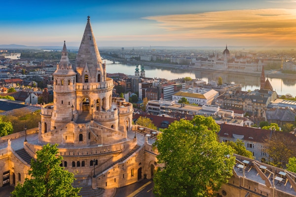 Budapest, Ungarn - Vakker gylden sommer soloppgang med tårnet til Fisherman's Bastion og grønne trær. Ungarns parlament og Donau i bakgrunnen. Blå himmel.