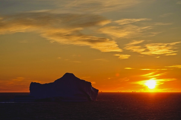 Et isfjell som driver i havet i solnedgangen