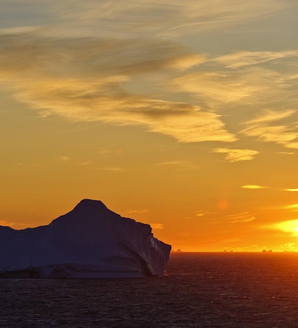 Et isfjell som driver i havet i solnedgangen