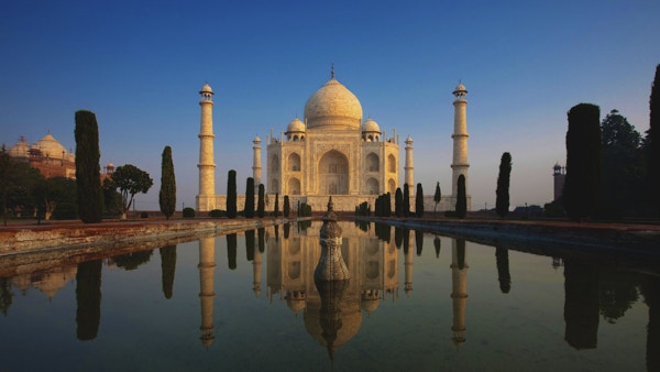 Taj Mahal lyser vakkert ved soloppgang, da den gjenspeiles i en rolig vannfontene.