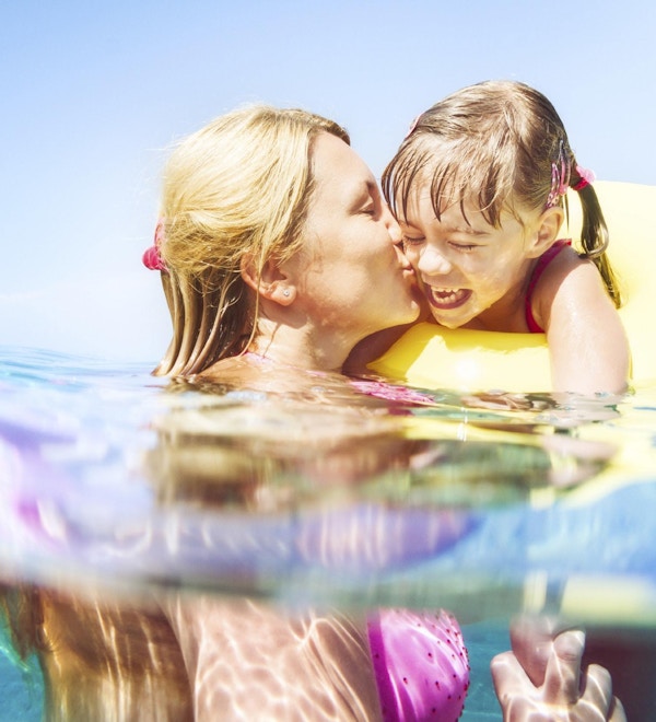 En ung jente og hennes mor svømmer i lyseblått vann på badeferie