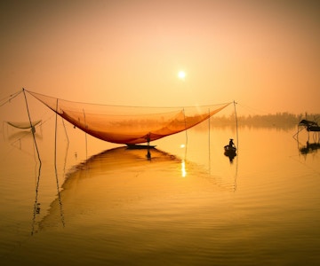 Uidentifisert fisker sjekker garnene sine tidlig om morgenen på elven i Hoian, Vietnam