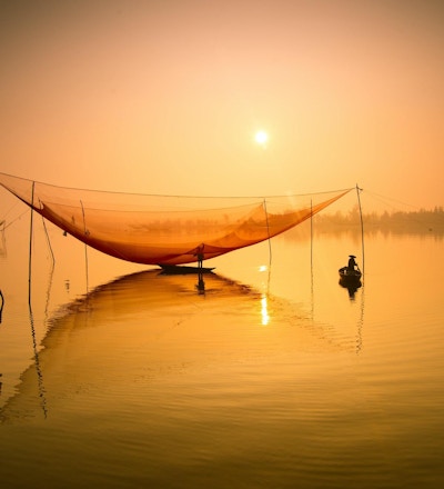 Uidentifisert fisker sjekker garnene sine tidlig om morgenen på elven i Hoian, Vietnam