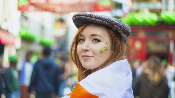 Smilende rødhåret irsk jente med ansiktsmalt og det irske flagget og tweedhetten i Temple Bar, Dublin, Irland