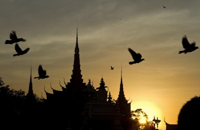 Solnedgangsutsikt over det kongelige palasset i Phnom Penh i Kambodsja med flygende fugler.