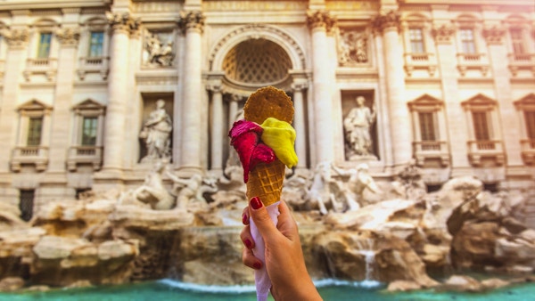 Hånd som holder fargerik gelato foran den berømte ikoniske Trevifontenen i Roma, Italia.