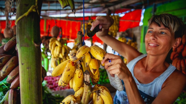 Smilende voksen kvinnelig turist som kjøper bananer på Bondens marked i Afrika.