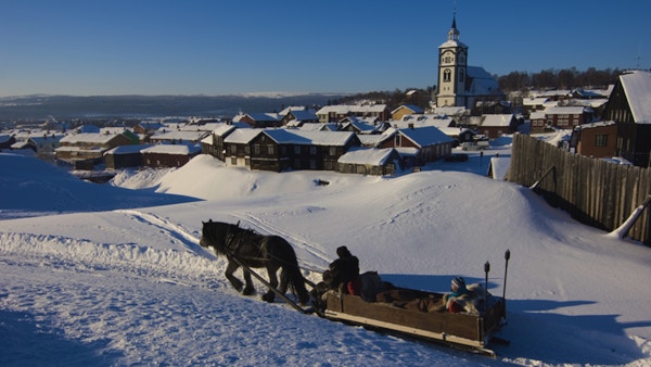 Hest og slede i vinterterreng med kirke og småhusbebyggelse i bakgrunnen