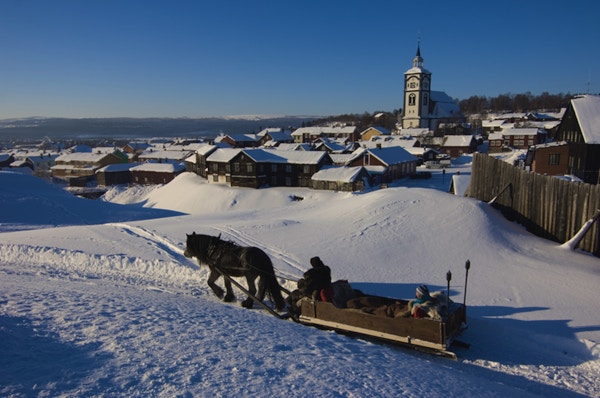 Hest og slede i vinterterreng med kirke og småhusbebyggelse i bakgrunnen