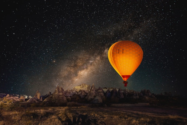 Varmluftsballong som flyr over spektakulære Cappadocia under himmelen med melkevei og skinnende stjerne om natten