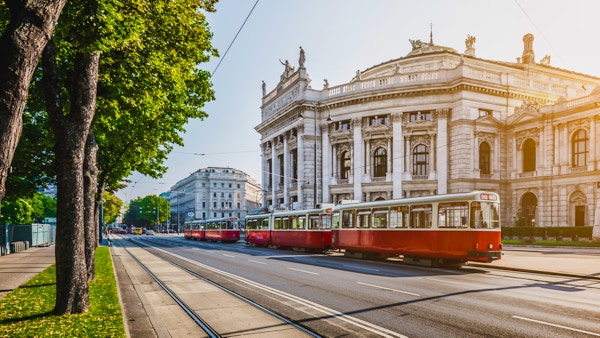 Den berømte Wiener Ringstrasse med det historiske Burgteateret (Imperial Court Theatre) og en tradisjonell rød, elektrisk trikk i soloppgang sett med retro vintage filtereffekt i Wien, Østerrike.