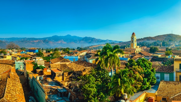 Panoramautsikt over byen Trinidad, Cuba med fjell i bakgrunnen og en blå himmel. Klokketårnet tilhører Iglesia y Convento de San Francisco.