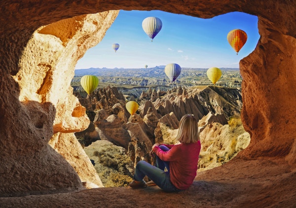 Kvinne som ser på fargerike varmluftsballonger som flyr over Cappadocia- dalen i Tyrkia. Vulkanske fjell i nasjonalparken Goreme.