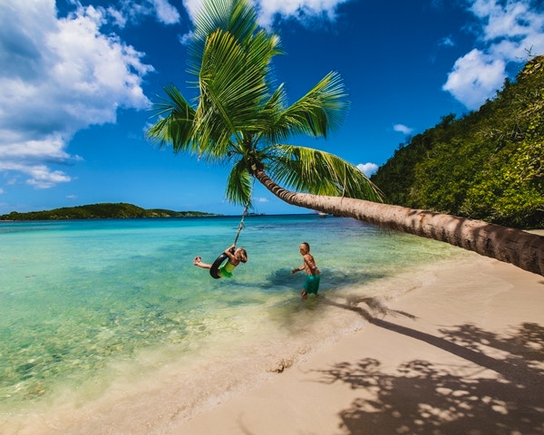 Karibisk strand med to personer som leker med en gummiring i en palme.
