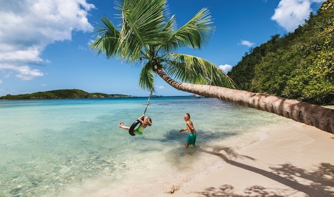 Karibisk strand med to personer som leker med en gummiring i en palme.