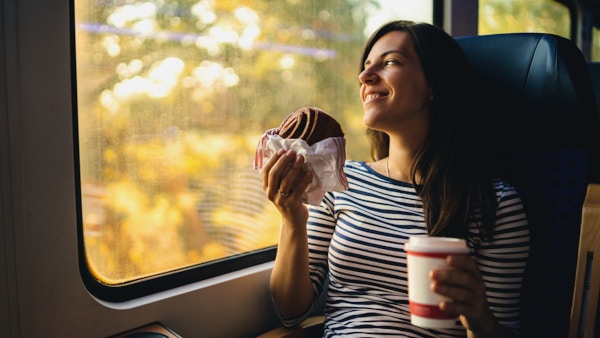 Ung kvinne spiser og beundrer utsikten fra et togvindu