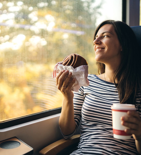 Ung kvinne spiser og beundrer utsikten fra et togvindu
