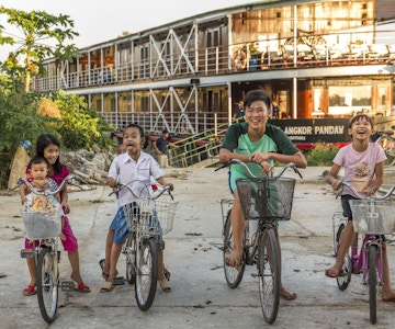 Smilende barn på sykler foran et elvecruiseskip i Vietnam. Foto.