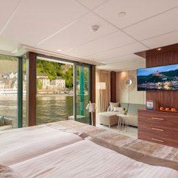 Oversikt over suite med seng, sittegruppe og panoramavindu mot elven.