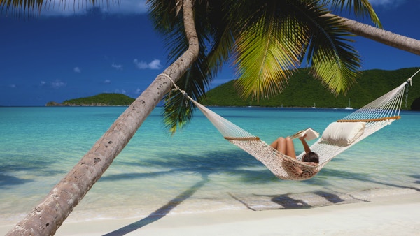 Kvinne som leser en bok i en hengekøye strukket mellom to palmer på en tropisk strand i Karibien
