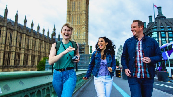 Tøffe voksne kaukasiske venner som har det gøy mens de utforsker Londons landemerker. De går forbi Palace of Westminster. De ser alle på hverandre mens de ler og suser gjennom byen. I bakgrunnen er det Elizabeth Tower. De har med seg ryggsekker og kamera.