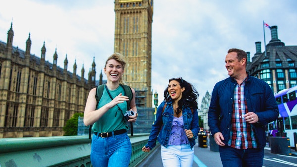 Tøffe voksne kaukasiske venner som har det gøy mens de utforsker Londons landemerker. De går forbi Palace of Westminster. De ser alle på hverandre mens de ler og suser gjennom byen. I bakgrunnen er det Elizabeth Tower. De har med seg ryggsekker og kamera.