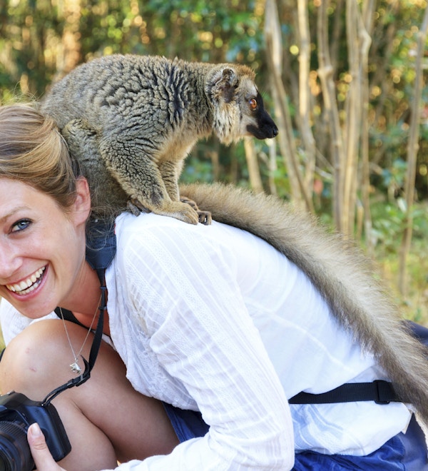 Kvinne med kamera som sitter på huk med en lemur på nakken