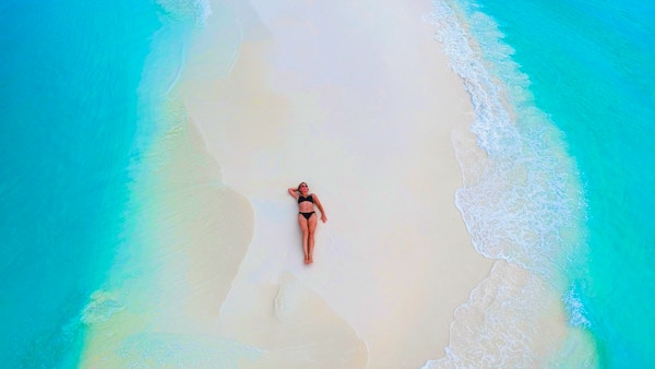 Vakker kvinne som ligger på sandbanken omgitt av turkis hav ovenfra