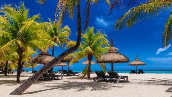 Paradisisk solrik strand med palmer og halmparasoller og tropisk hav på øya Mauritius.