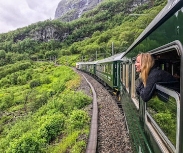 Kvinne ser ut av togvindu mens toget kjører gjennom grønt fjellandskap.