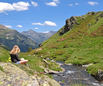 "To jenter som sitter ved en bekk og ser på vannet, i Pyrenees-fjellene i Andorra"