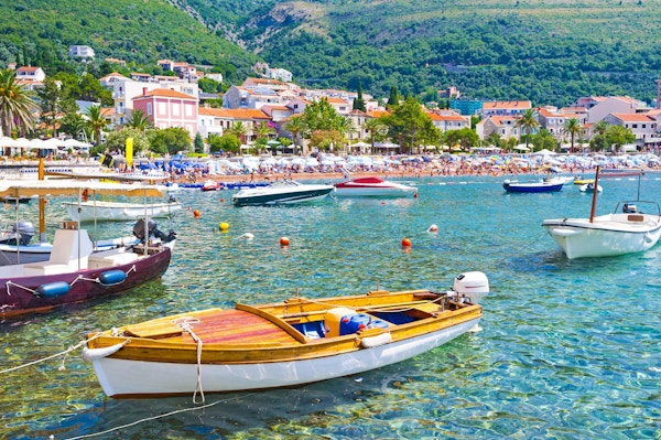 De små båtene i fortøyd havn med den offentlige stranden i bakgrunnen, Petrovac, Montenegro.