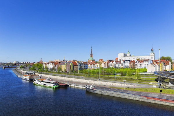 Stor elvepram og sightseeingskip fortøyd til vollen på elven Odra med gamlebyen i Szczecin i bakgrunnen