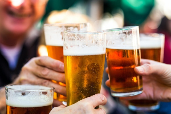 Nærbilde fargebilde som viser en gruppe mennesker som feirer med en skål. Folket jubler glassene sine øl (halvliter øl) sammen i en gest av feiring, samvær og lykke. Folket er fokusert i bakgrunnen, mens fokuset er på ølglassene i forgrunnen. Rom for kopiplass.