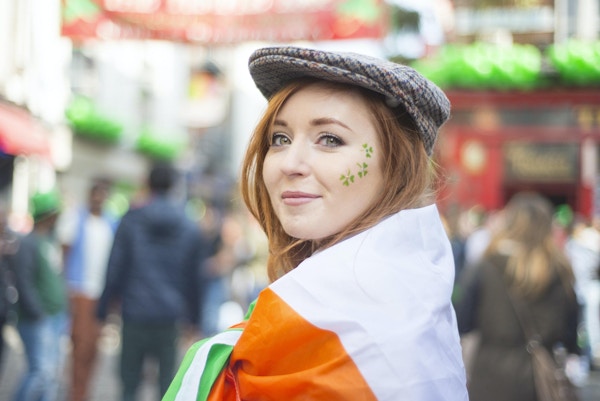 Smilende rødhåret irsk jente med ansiktsmalt og det irske flagget og tweedhetten i Temple Bar, Dublin, Irland