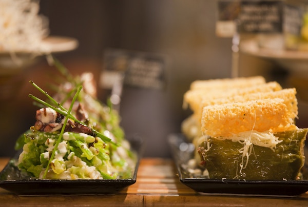 Spanske Tapas, eller, i Baskerland, Pintxos, uttales “Pinchos” i foodie-hovedstaden i Spania, San Sebastian, på en bar i Mercado La Brexta-matmarkedet. På venstre side, blekksprut salat og grønnsaker, og til høyre, Green Pepper fylt med kjøtt.
