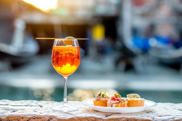 Spritz Aperol drink med venetianske tradisjonelle snacks cicchetti på vannkanalen bakgrunn i Venezia. Tradisjonell italiensk aperitiff. Bilde med liten dybdeskarphet