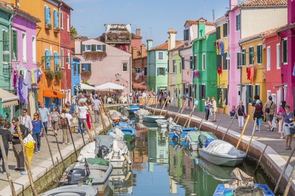Burano, Italia - 2. oktober 2014: Flerfargede hus stiller gater og kanaler på øya Burano nær Venezia. Øya er et populært turiststed. Vi ser folk gå langs kanalen der det er butikker, restauranter og typiske hus på torget.