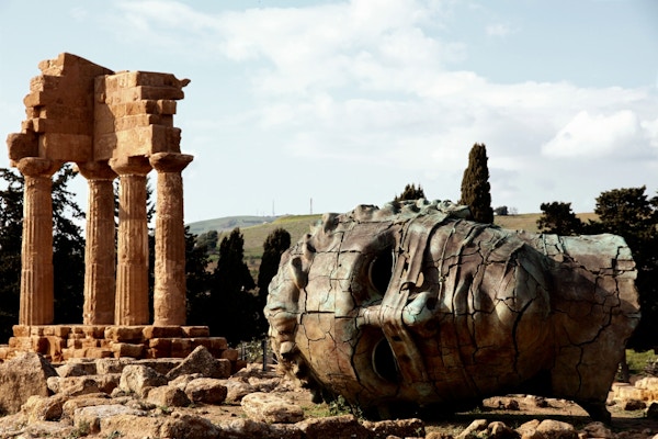 Bronsehodet til en kolossusstatue foran de gamle greske tempelruinene av Castor og Pollux på det arkeologiske området til tempeldalen som ligger i Agrigento, Sicilia. Italia.