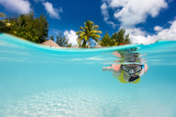 Kvinne svømmer under vann i klart tropisk vann foran eksotisk øy
