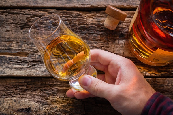 hånd holder whisky i et glass for å smake på en trebakgrunn