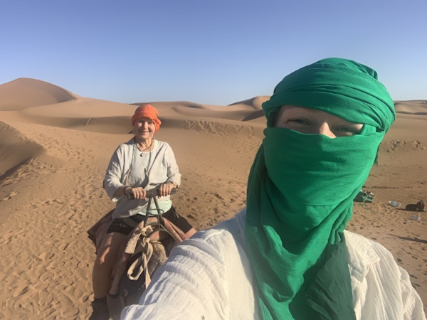 To turbankledde damer rir på kamel i saharaørkenen