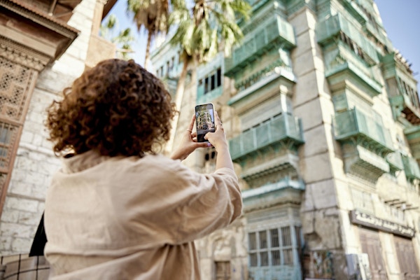 Utsikt i lav vinkel bak brunette kvinne mens hun fanger et minne med smarttelefon mens hun reiser i Al-Balad, Saudi-Arabia.