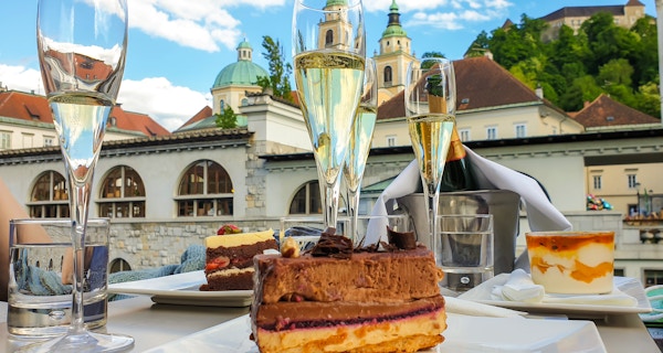 Nærbilde av glass champagne og kaker ved Trippelbropromenaden ved elven Ljubljanica.