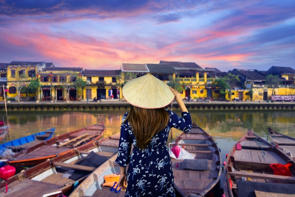 Kvinneturist har tradisjonell vietnamesisk Non La-hatt og ser på vakker utsikt ved elvebredden i gamlebyen Hoi An i Vietnam under solnedgangsskumring.