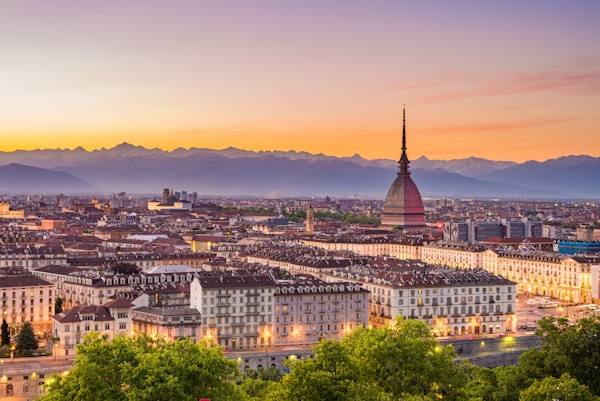 Bybildet i Torino (Torino, Italia) i skumringen med fargerik humørfylt himmel. Mole Antonelliana ruver på den opplyste byen nedenfor.