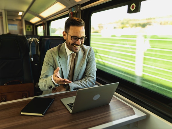 Ung forretningsmann som reiser til jobben med tog, jobber mens han reiser, med den bærbare datamaskinen og notatboken, snakker i telefon