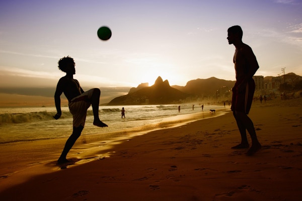 To menn som spiller fotball på en strand i Rio de Janeiro i solnedgangen.